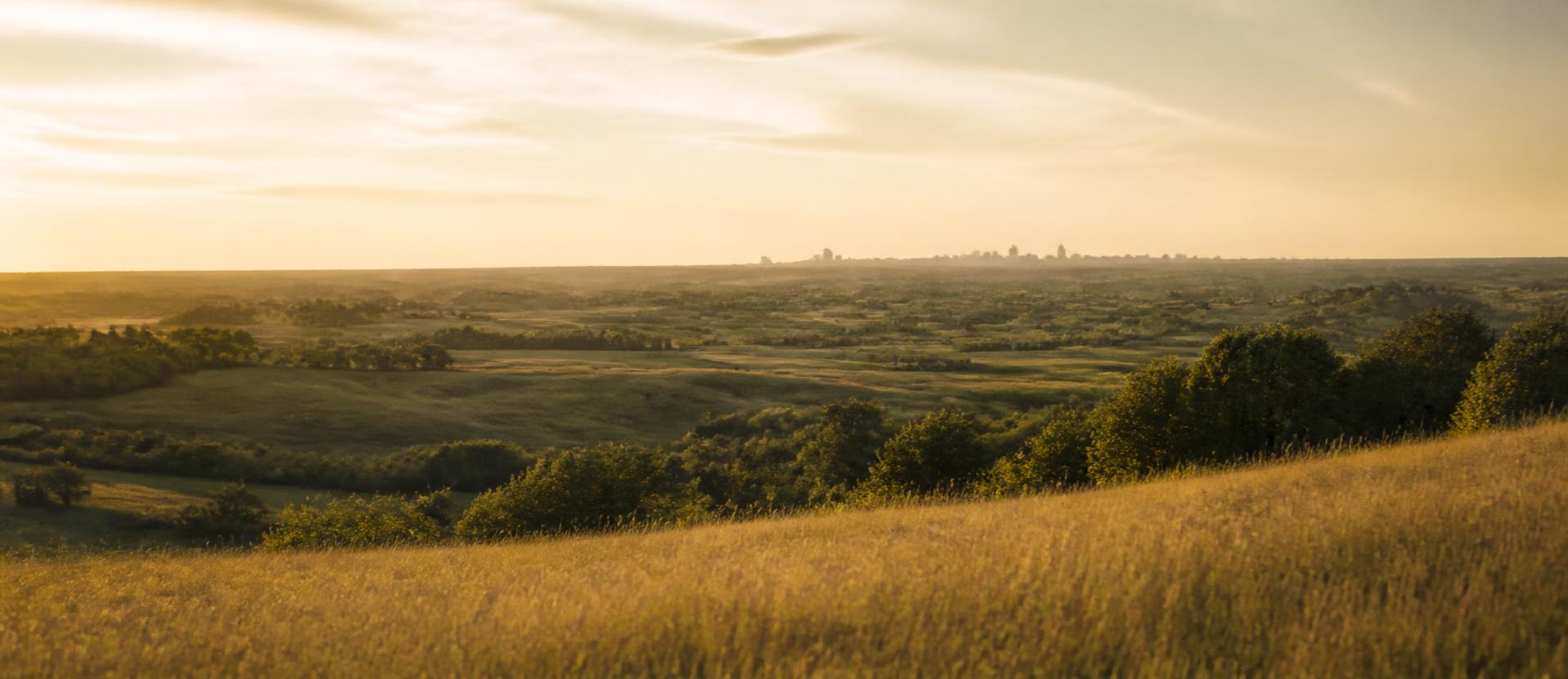 Rolling prairie at golden hour with a distant Kansas City skyline